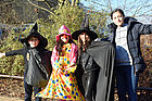 Vier Kinder, davon zwei als Zauberer und eins als Clownin verkleidet, posieren vor ihrer Schule mit ausgebreiteten Armen.