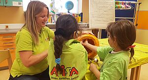 Die Erzieherin Jutta Heim und zwei Kinder untersuchen einen aufgeschnittenen Kürbis