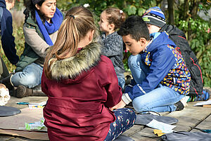 Mehrere Kinder sitzen draußen in der Natur auf dem Boden