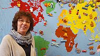 Kitaleiterin Monika Schäfer steht vor einer Weltkarte für Kinder