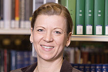 Porträt von Dr. Iren Schulz, einer Frau mit dunkelblonden Haaren, vor einem Bücherregal.