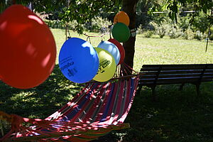 Eine Hängematte wischen zwei Bäumen, darüber eine Girlande aus bunten Luftballons