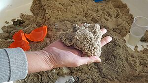 Eine Hand voll Sand über einem Sandkasten