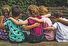 Fünf Kinder sitzen nebeneinander, die Arme um die Schulter ihrer Sitznachbarn gelegt