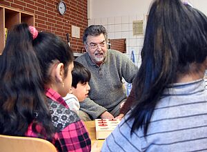 Holger Gutt sitzt mit den Schülern seiner Vorklasse am Tisch und spielt ein Sprachlernspiel
