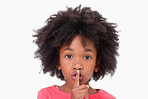 Ein Kind hält sich den Zeigefinger vor den Mund, um die Aufforderung zum Schweigen mit einer Geste darzustellen