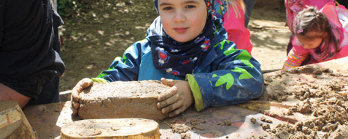 Ein kleiner Junge nimmt einen frisch geformten Lehmziegel in die Hände.