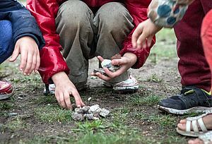 Kinder hocken auf der Wiese und halten Steine und Kiesel in den Händen
